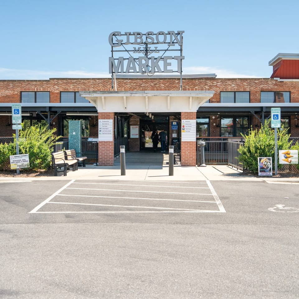 Exterior view of Gibson Mill Market entrance with a sign listing Thai Esane among other businesses.