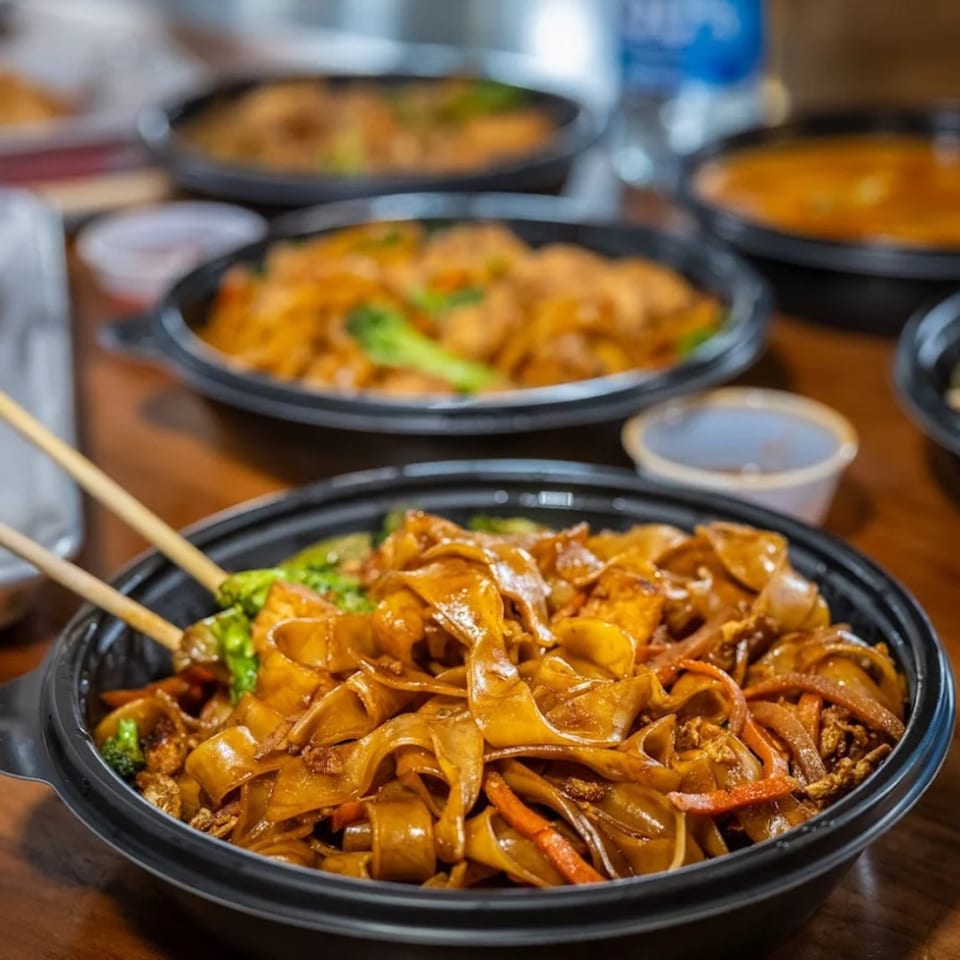 Multiple black bowls of Thai Esane's Pad See Ew with chopsticks, ready for takeout.