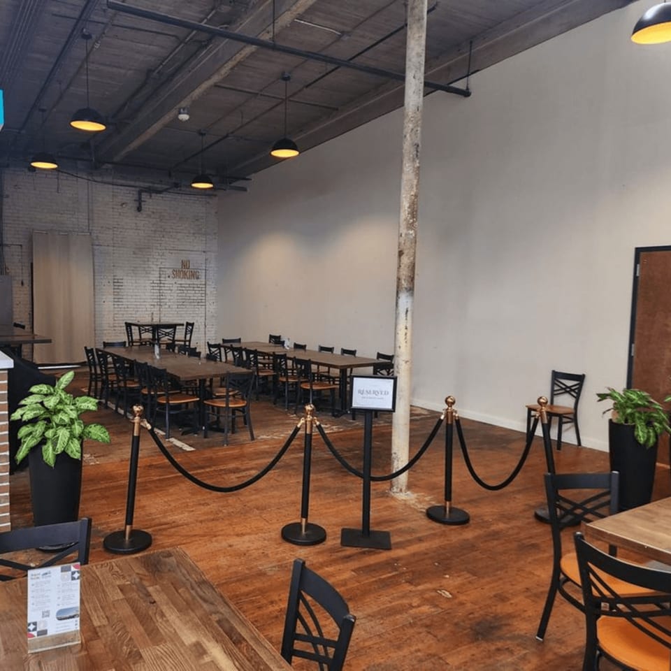 Thai Esane's dining room with long wooden tables, black chairs, and stanchions with a "Reserved" sign.