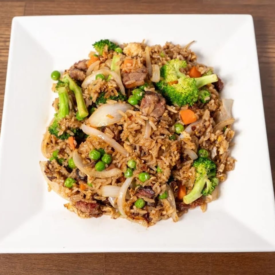 Thai Esane's fried rice with beef, broccoli, peas, carrots, and onions on a white plate.