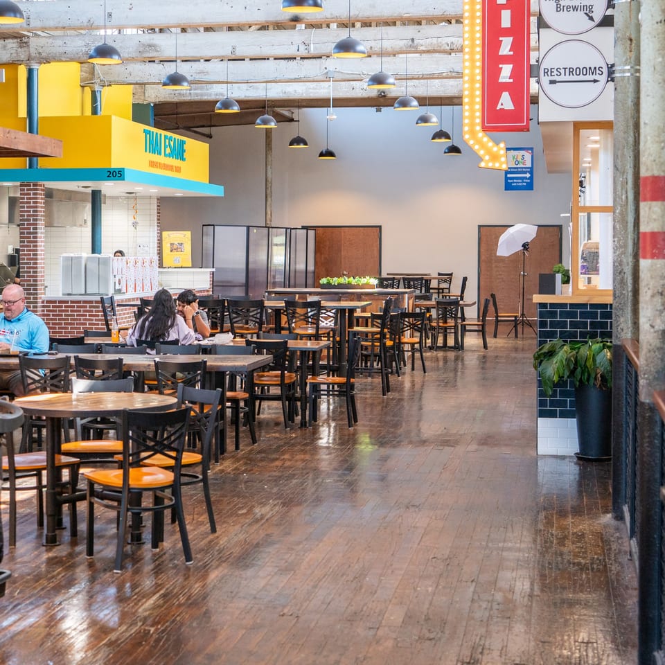 The interior of Thai Esane restaurant with tables, chairs, and a few patrons, under industrial lighting.