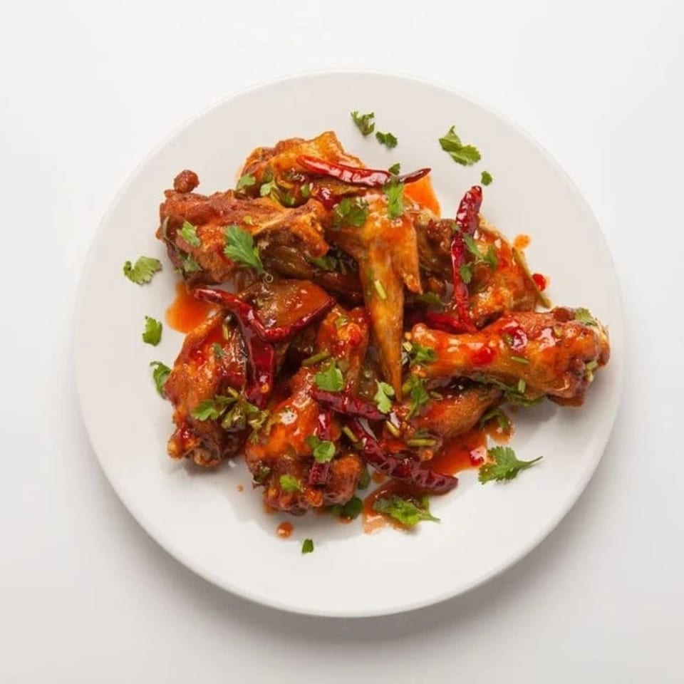 Thai Esane's spicy chicken wings, garnished with red chilies and fresh cilantro on a white plate.